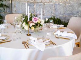 Boda banquete concepto. sillas y redondo mesa para huéspedes, servido con cuchillero y, flores y vajilla y cubierto con un Manteles foto