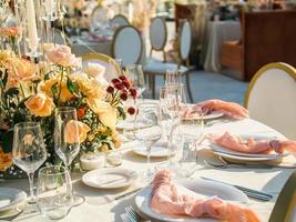 Beautiful outdoor wedding decoration in city. Candles and dried flowers and accessories with bouquets and glasses on table with linen tablecloth on newlywed table on green lawn photo