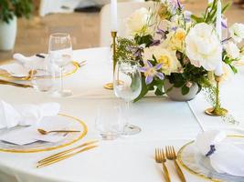 Boda banquete concepto. sillas y redondo mesa para huéspedes, servido con cuchillero y, flores y vajilla y cubierto con un Manteles foto