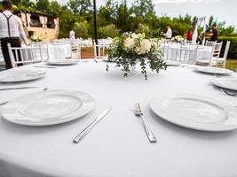 Wedding banquet concept. Chairs and round table for guests, served with cutler and, flowers and crockery and covered with a tablecloth photo