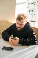 Portrait happy guy making money transaction via application on mobile phone with 4g internet sitting at cafe in street evening, serious millennial man reading text message on smartphone photo