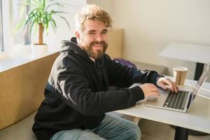 Smiling male guy resting in coffee shop chatting in social networks skilled freelancer enjoying remote job typing publication for web blog on laptop photo