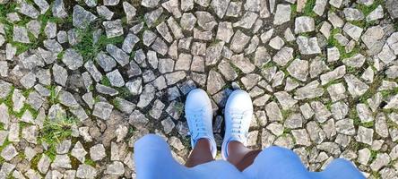 background of female legs with white sneakers and dress on a stone floor photo