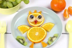 Fun food for kids. Cute appetizing fresh fruit chicken - orange, banana, blueberry - for a healthy breakfast with milk and biscuits photo