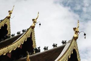 Golden naga and bells hanging on Art Roof of Buddhist temple with blue sky in Thailand photo