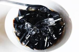 tailandés dulce postre césped jalea con hielo en blanco bol. un tipo de chino vegetal es negro jalea o hierbas lata aliviar calor en humano cuerpo sistema y aftoso estomatitis en Hora de verano. foto