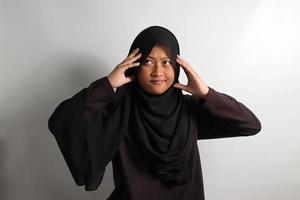 Young Asian girl in headscarf grabbing her head with serious expression photo