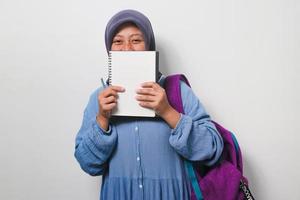 Young Asian girl student in hijab covering her face with book isolated on white background. photo