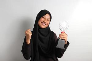 inteligente joven asiático niña estudiante en hijab levantamiento su trofeo aislado en blanco antecedentes. foto