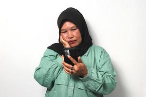 medio Envejecido asiático mujer vistiendo hijab mirando a su teléfono galería extraña su niño foto