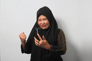Excited Middle aged Asian women wearing hijab looking at her phone with YES gesture getting good news photo
