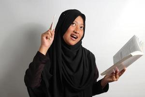 Excited young Asian girl holding a book and pen got an idea isolated on green background photo