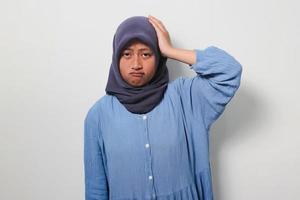 Young Asian girl in hijab grabbing her head while thinking about something photo