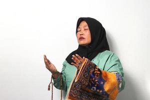 Middle aged Asian women wearing hijab prays to God and holding prayer beads and player mat isolated over white background. photo