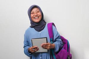 Clever young Asian girl student in hijab holding a pen and book on white background. photo