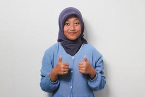 Cheerful young Asian girl in hijab showing two thumbs up photo