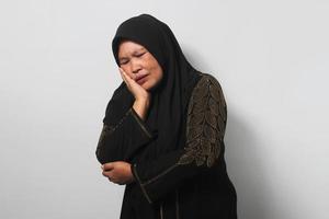 medio Envejecido asiático mujer vistiendo hijab conmovedor boca con mano con doloroso expresión porque de dolor de muelas o dental enfermedad en dientes foto