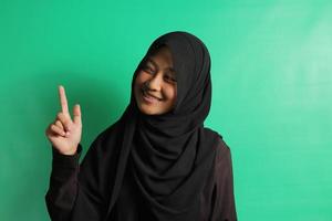 Young Asian girl pointing fingers on the left on green background. photo