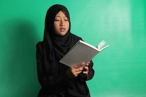 Surprised young Asian girl reading a book over green background photo