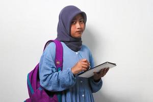 joven asiático niña estudiante en hijab escritura alguna cosa en el libro aislado en blanco antecedentes. foto