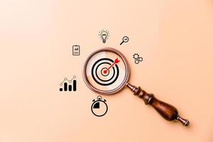 Hand holding target board inside vintage magnifying glass for focus business objective on orange background and copy space. Search, goal, strategy, success. successful marketing strategy goals photo