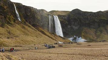 Groups of tourist visiting walk on pathways by beautiful waterfall of Seljalandsfoss in spring video