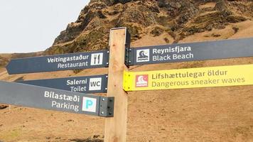 Wooden signpost with directions arrows to attractions on black sand beach in Reynisfjara . Iceland navigation and information signs video
