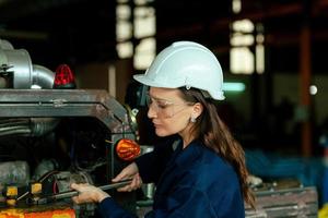 un contento joven mujer trabajador de un grande maquinaria mantenimiento fábrica en un azul vestir y un blanco protector sombrero. mantenimiento mantenimiento. fábrica seguridad. bandera imagen foto