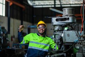 Portrait of an African American engineer standing with his arms crossed, inspecting and controlling an automated welding robot. The robotic arm in the automotive factory is smart. photo