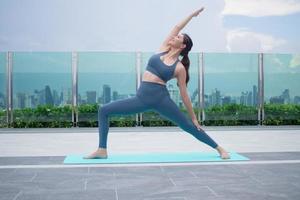 mujer delgada practicando yoga en el balcón de su condominio. mujer asiática haciendo ejercicios por la mañana. equilibrio, meditación, relajación, calma, buena salud, feliz, relax, concepto de estilo de vida saludable foto