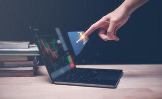 investment in stock market concept, financial investment strategy, man pointing to virtual trading graph buy and sell price with computer laptop on wood table photo