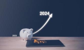 saving and investment plan for 2024 concept, piggy bank and virtual arrow up trend from 2023 to 2024 photo