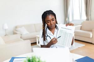 Smiling professional female doctor wearing uniform taking notes in medical journal, filling documents, patient illness history, looking at laptop screen, student watching webinar photo