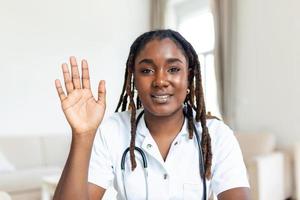 African oman doctor talking online with patient, making video call, looking at camera, young female wearing white uniform with stethoscope speaking, consulting and therapy concept photo