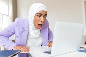 Confused Arabic muslim businesswoman annoyed by online problem, spam email or fake internet news looking at laptop, office worker feeling shocked about stuck computer photo