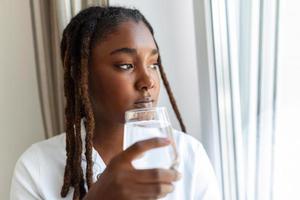 Young African woman in casualwear drinking water from glass photo
