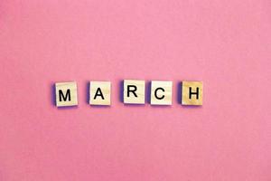 inscription March made by wooden cubes on a pastel pink background. photo