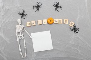 inscription halloween,spider web and spiders on gray background with skeleton and paper sticker photo