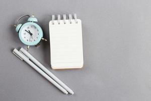 Top view of blank note paper with pen and alarm clock on gray background photo