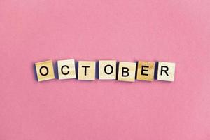 inscription October made by wooden cubes on a pastel pink background. photo