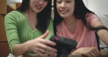 Footage of Happy Asian young women unpacking cardboard boxes while sitting on the floor in new apartment. Moving and lifestyle concepts. video