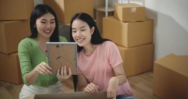 beeldmateriaal van gelukkig Aziatisch jong Dames uitpakken karton dozen terwijl zittend Aan de verdieping in nieuw appartement. in beweging en levensstijl concepten. video