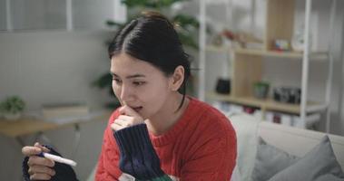 imágenes de cerca de contento asiático joven mujer mirando a el embarazo prueba en felicidad mientras sentado en sofá a el vivo habitación. el embarazo o familia conceptos. video