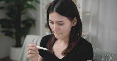 Footage close-up of Unhappy Asian young woman shocked at positive pregnancy test result while sitting on couch at the living room. Pregnancy or health problem concepts. video