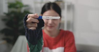 Footage close-up of Happy Asian young woman looking at pregnancy test in happiness while sitting on couch at the living room. Pregnancy or family concepts. video