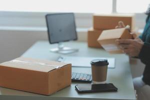 Startup SME small business entrepreneur of freelance Asian woman wearing apron using laptop and box to receive and review orders online to prepare to pack sell to customers, online sme business ideas. photo