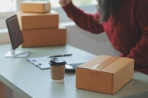 Startup SME small business entrepreneur of freelance Asian woman wearing apron using laptop and box to receive and review orders online to prepare to pack sell to customers, online sme business ideas. photo