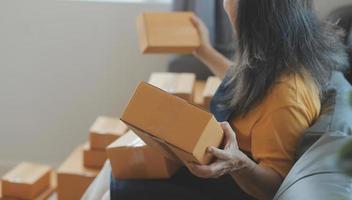 Startup SME small business entrepreneur of freelance Asian woman wearing apron using laptop and box to receive and review orders online to prepare to pack sell to customers, online sme business ideas. photo