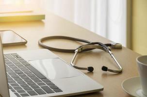 Stethoscope on Doctor desk with labtop, smartphone, file folder and coffee cup in doctor room, focus on stethoscope. Healthcare concept. photo