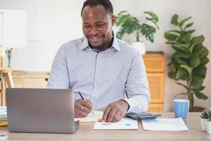 African American businessman of black descent sits smiling and doing financial reports and studying annual profit analysis An accountant checking the financial status of the company is in the office. photo